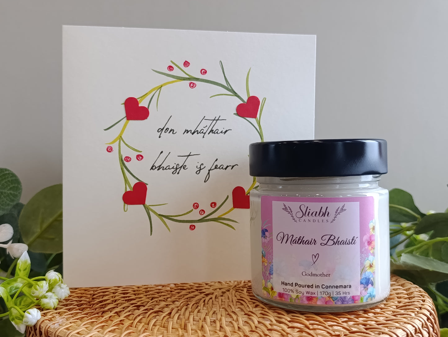 Candle jar with a decorative card on a textured surface. Máthair Bhasití - Godmother Candle