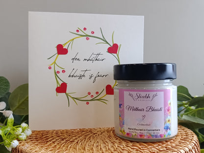 Candle jar with a decorative card on a textured surface. Máthair Bhasití - Godmother Candle
