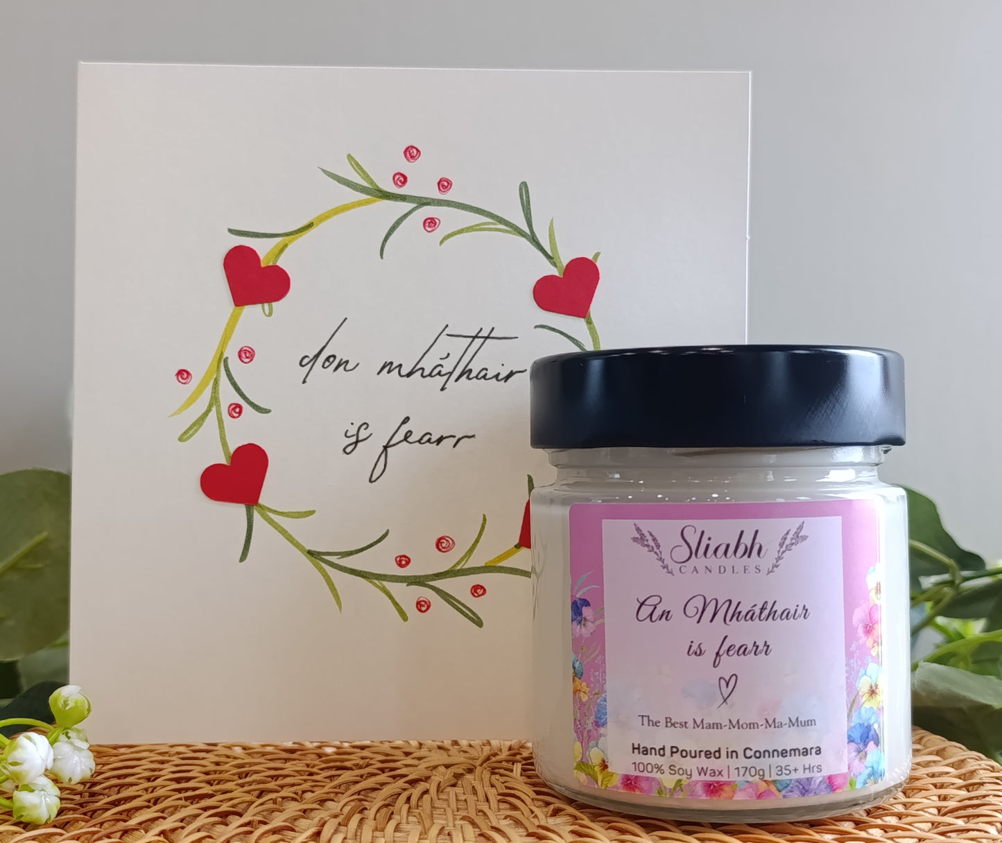 Jar of soy wax candle from Sliabh candles with a decorative card featuring hearts and text on a textured surface. An Mháthair is fearr which means the best mam. 