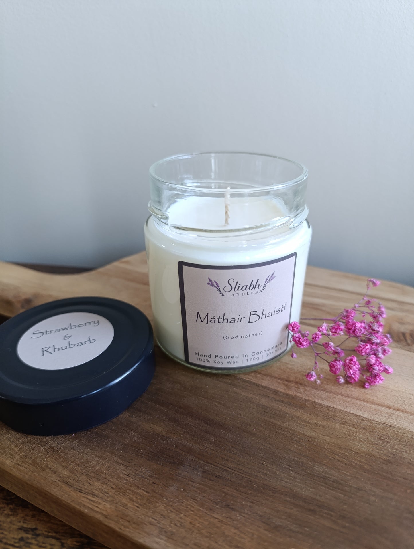 Candle in a glass jar with a Godmother in Irish label on a wooden surface