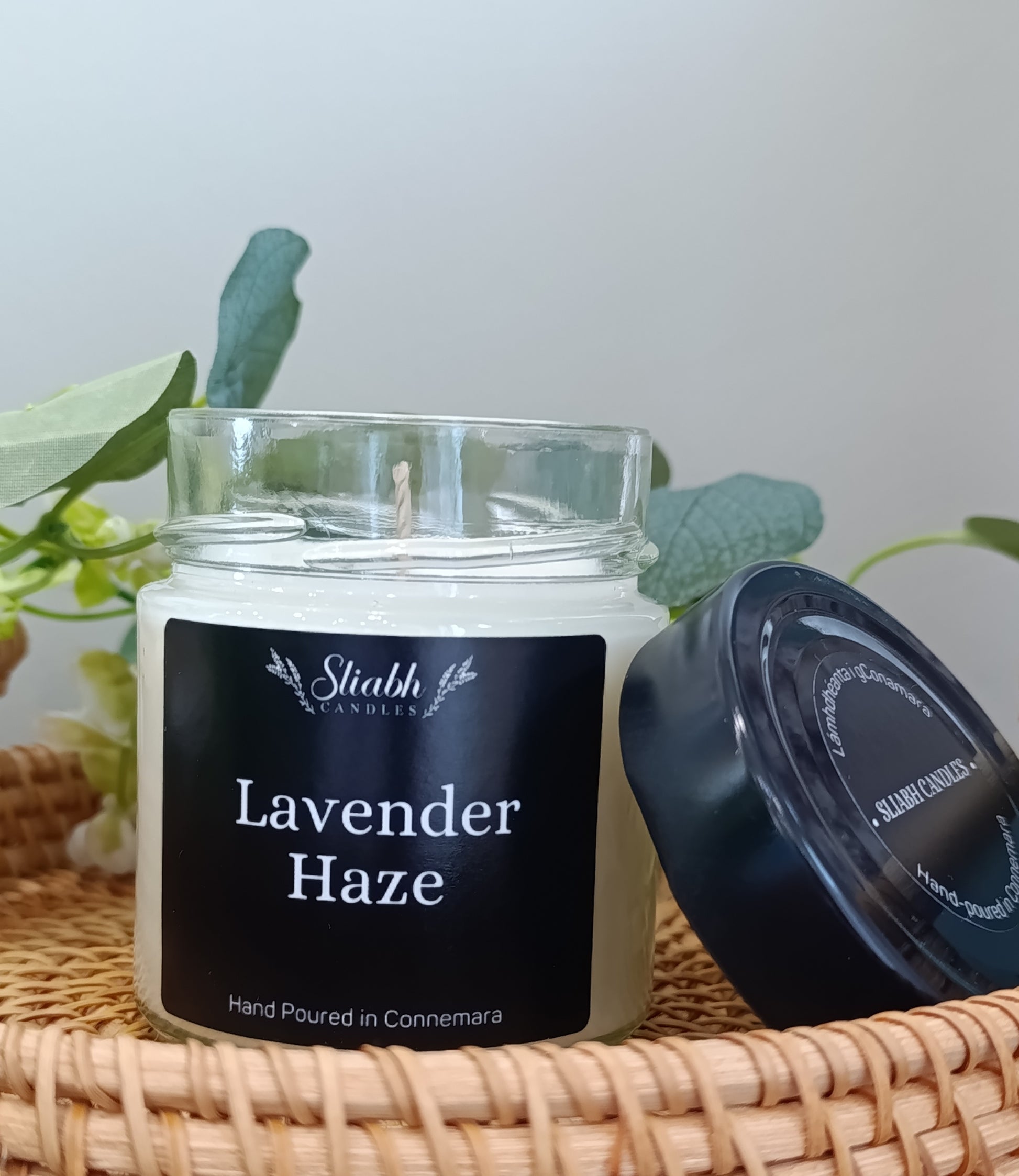 Candle jar labeled 'Lavender Haze' by Stiabh Candles on a woven surface with plants in the background.