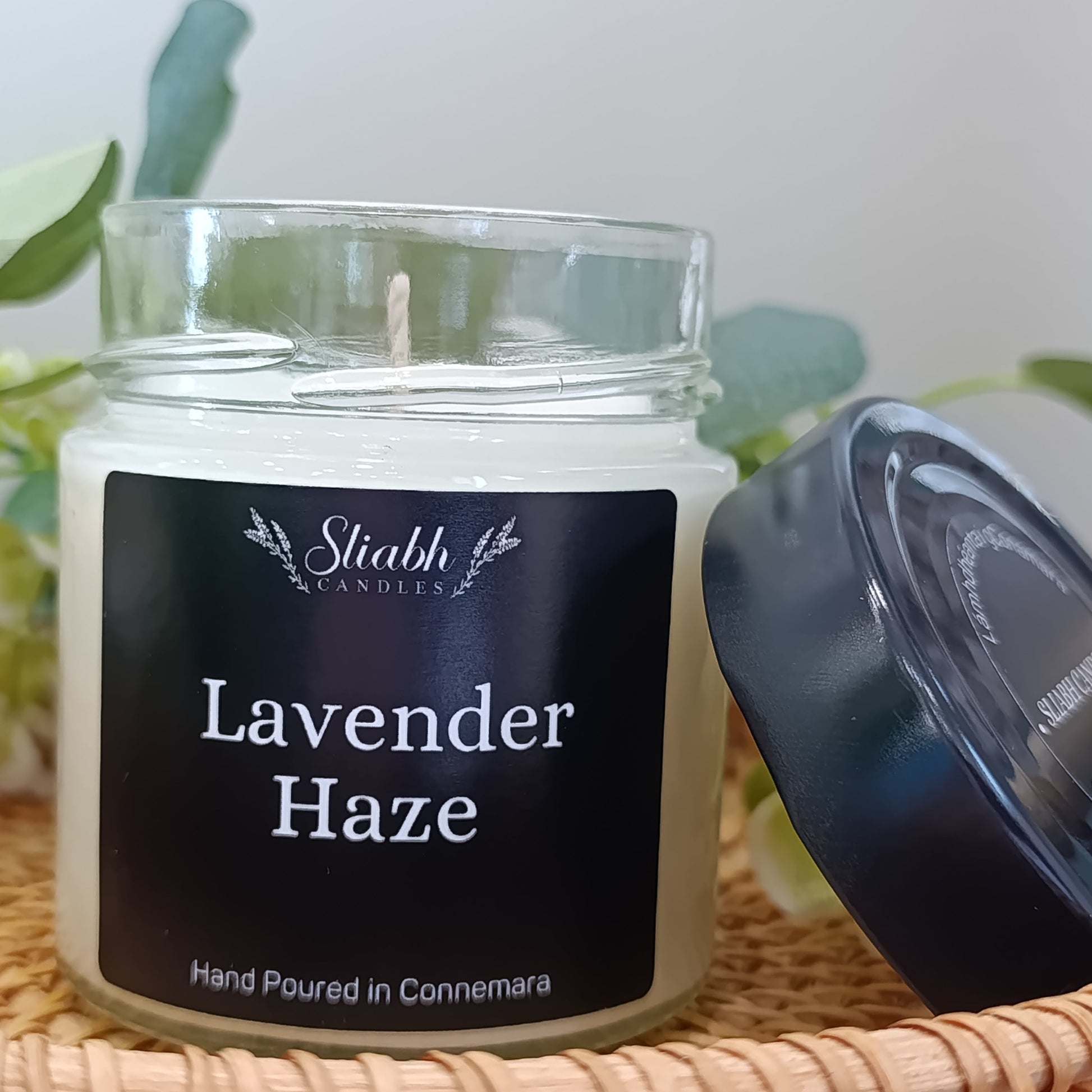 Candle jar labeled 'Lavender Haze' by Stiabh Candles on a woven surface with a plant in the background.
