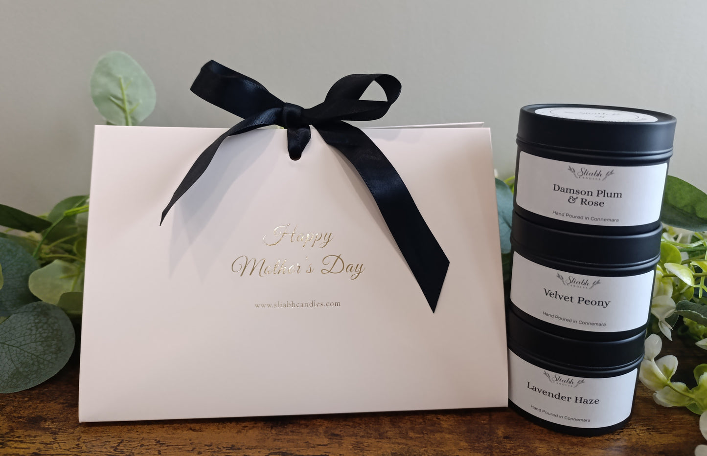 White gift box with black ribbon and 'Happy Mother's Day' text, next to stacked candles on a wooden surface. Set of 3 soy wax candles.