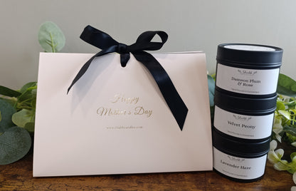 White gift box with black ribbon and 'Happy Mother's Day' text, next to stacked candles on a wooden surface. Set of 3 soy wax candles.