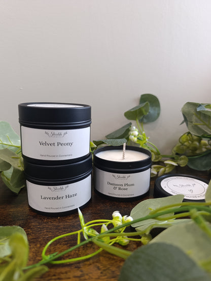 Three candles with labels on a wooden surface surrounded by green leaves