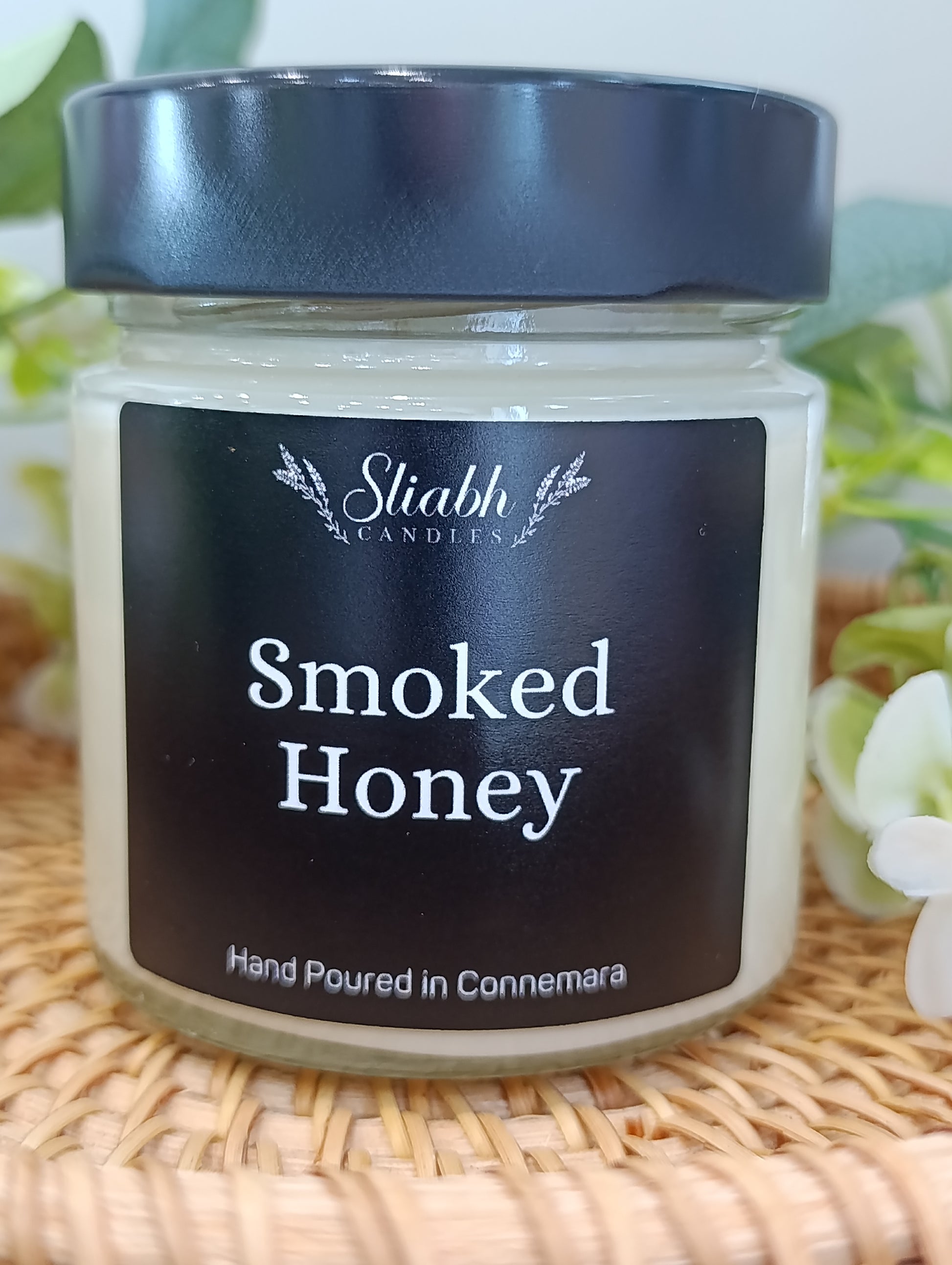 Jar of 'Smoked Honey' candle with a black lid on a woven surface.