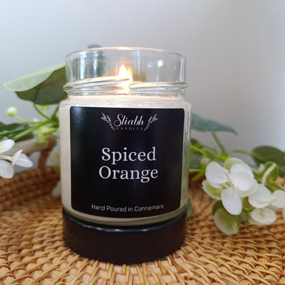 Candle labeled 'Spiced Orange' by Stiabh Candles on a woven surface with flowers.