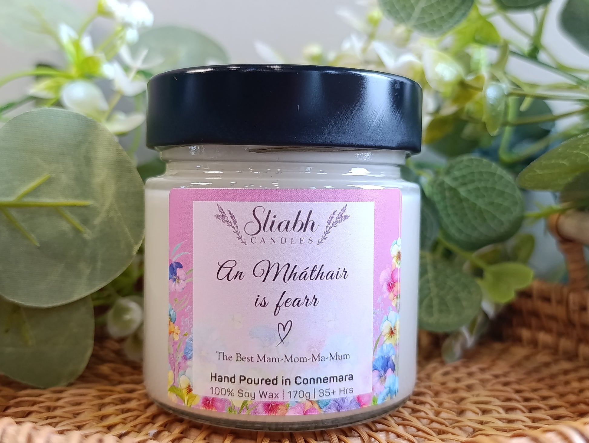 Jar of Sliabh candles with decorative label on a woven surface with plants in the background. Scented Soy wax Candle with the Best Mam 