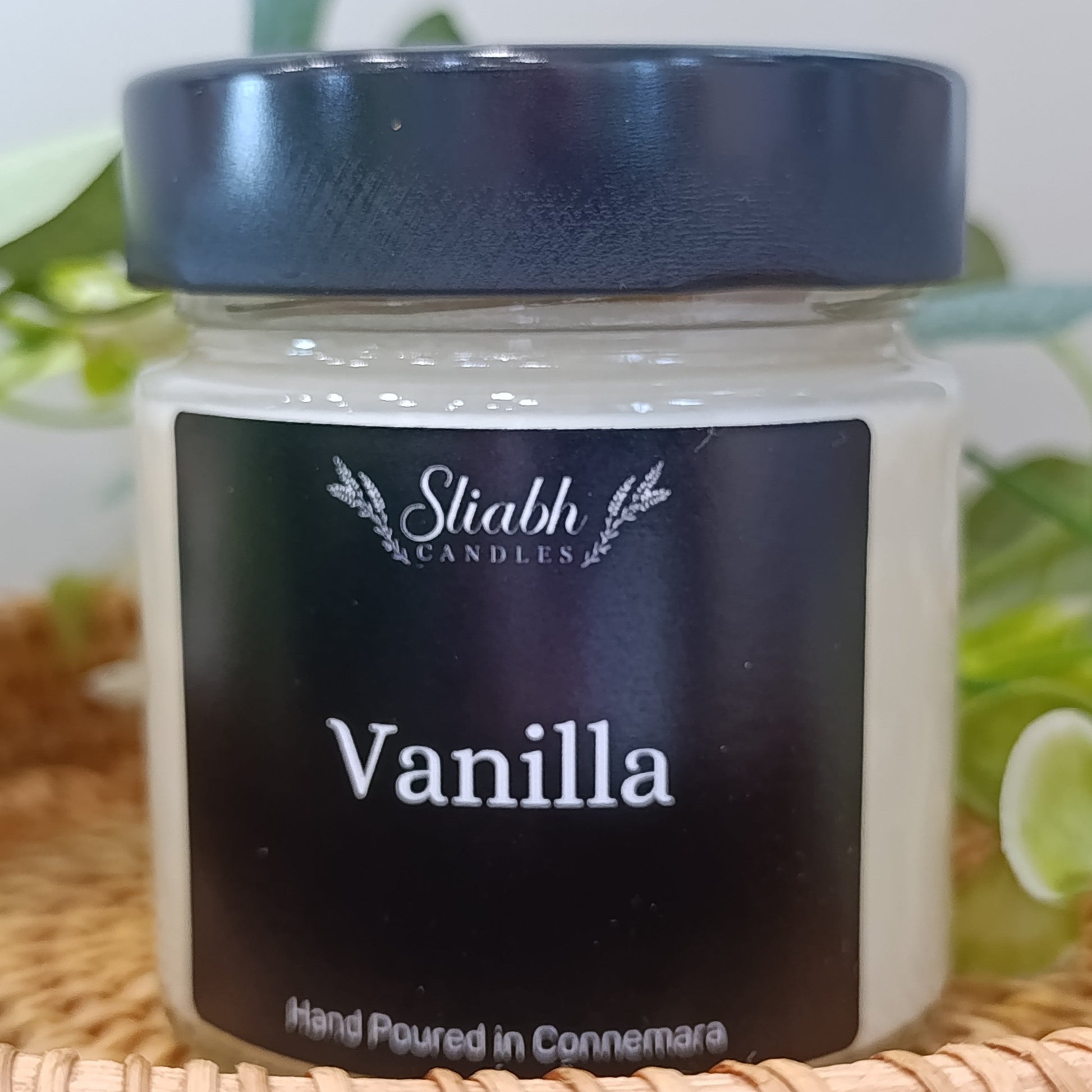 Jar of vanilla candle with 'Sliabh Candles' branding on a woven surface.